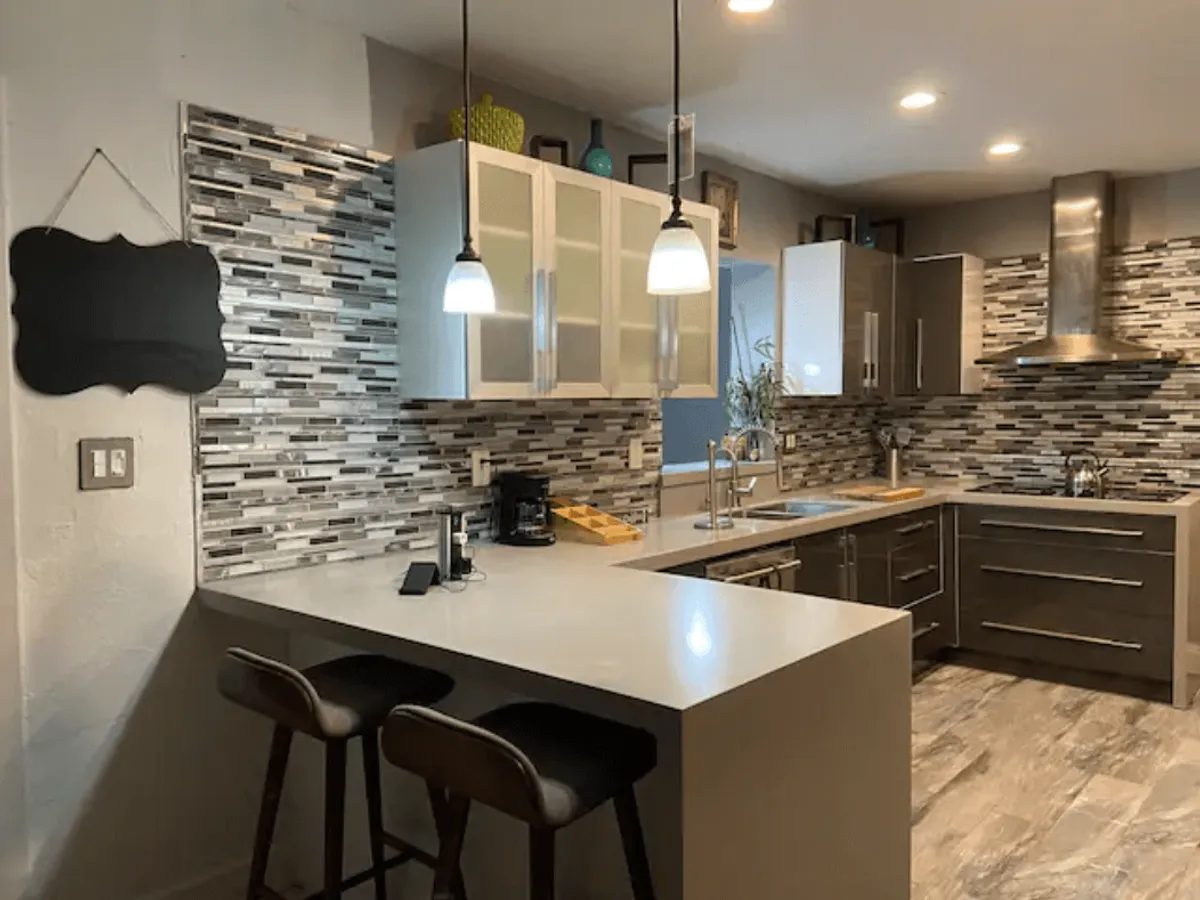 A sleek and functional kitchen with a central island, pendant lighting, modern cabinetry, and a decorative backsplash. The generous counter seating makes it ideal for casual breakfasts or chatting with friends while preparing food.