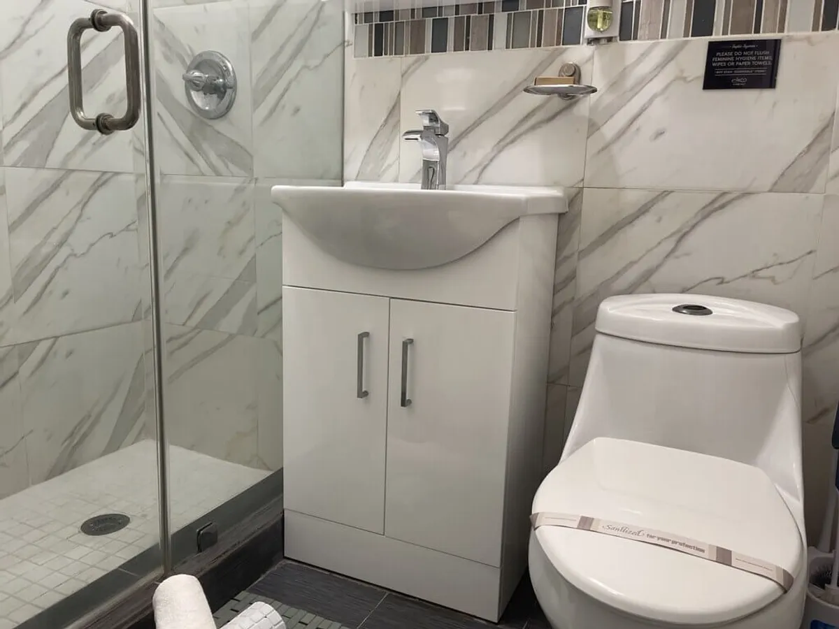 A modern bathroom featuring a glass-enclosed shower with chrome handle, a white vanity with integrated sink, and a modern toilet. The space is clean, bright, and inviting, emphasizing comfort and hygiene.